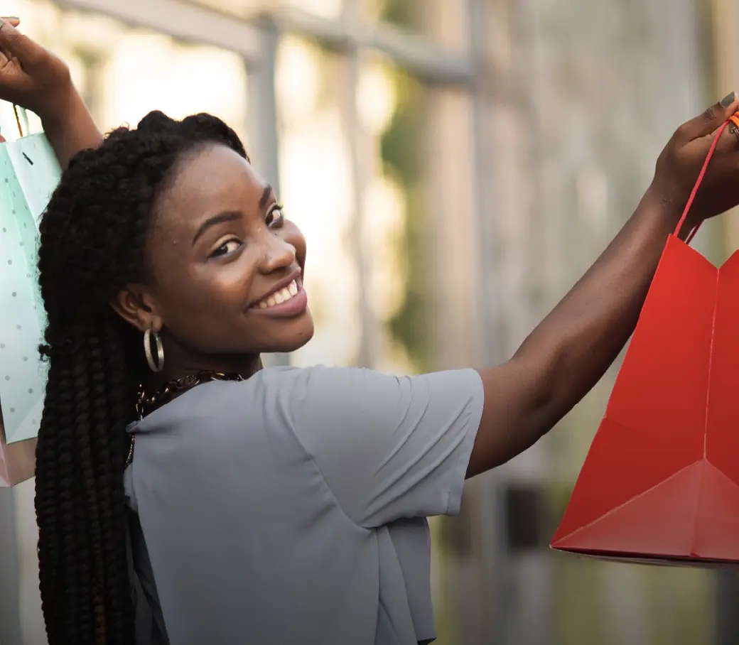 A shopper smiling over her shoulder, holding a red shopping bag